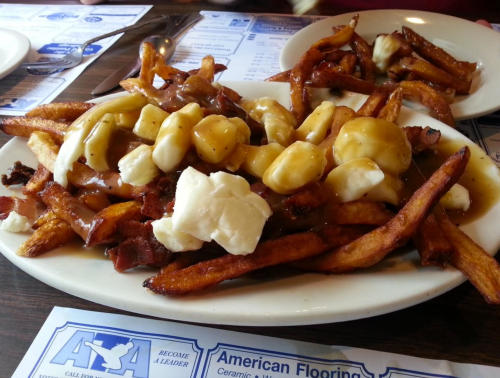 A plate of poutine topped with bacon, featuring fries, cheese curds, and gravy.