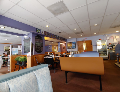 Interior of a cozy diner with booths, tables, and a chalkboard menu, featuring purple walls and casual decor.