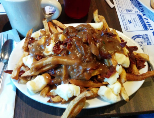 A plate of poutine topped with gravy, cheese curds, and crispy bacon, served with fries.