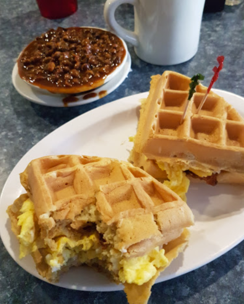 A plate with two waffle sandwiches filled with eggs, alongside a bowl of chili.