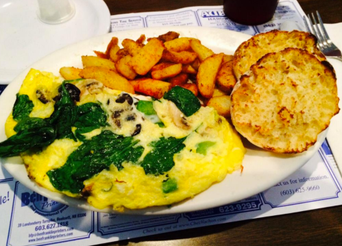 A plate with a spinach and mushroom omelet, seasoned potatoes, and toasted English muffin halves.