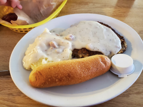 A plate with fried chicken covered in gravy, mashed potatoes, and a corn dog, served with a small cup of sauce.