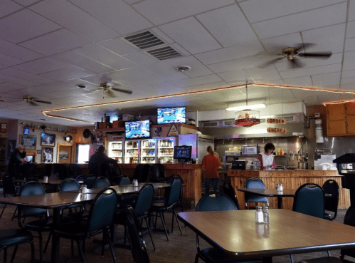 Interior of a casual diner with tables, a counter, and two TVs showing sports. Warm lighting and a cozy atmosphere.