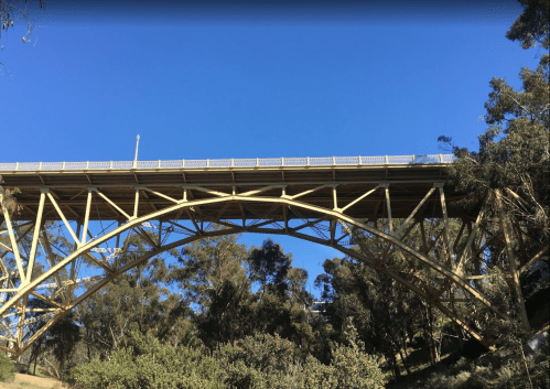 A large yellow bridge arches over trees against a clear blue sky.