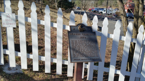 A historical marker for Flower Cemetery, surrounded by a white picket fence, with a "No Dogs Allowed" sign nearby.
