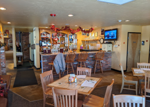 Cozy restaurant interior with a bar, wooden tables, and festive decorations. A TV is visible in the background.