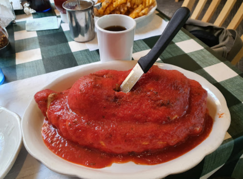 A large, oval-shaped meat dish covered in red sauce, served on a white plate with a knife resting on top.