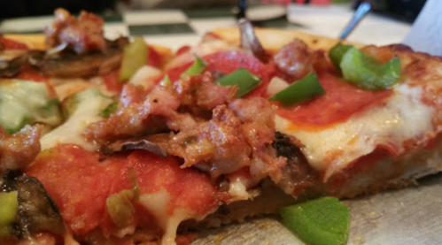Close-up of a slice of pizza topped with pepperoni, sausage, green peppers, and mushrooms on a crust.