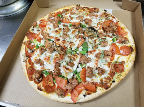 A large pizza topped with pepperoni, sausage, mushrooms, tomatoes, and green peppers in a cardboard box.
