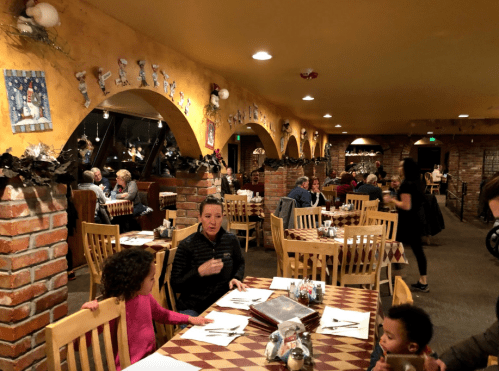 A cozy restaurant interior with families dining, featuring brick walls and festive decorations.