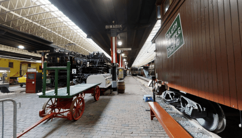 Interior view of a train museum featuring vintage locomotives and rail cars, with brick flooring and overhead lighting.