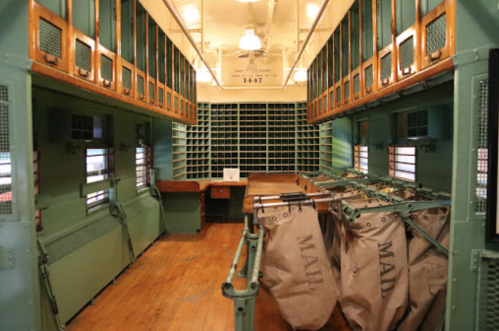 Interior of a vintage mail car with green walls, wooden accents, and large mail bags.
