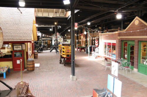 A vintage-style indoor market with colorful storefronts, brick pathways, and rustic decor.