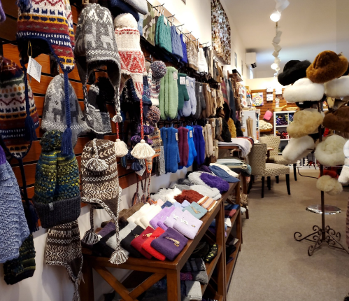 A cozy shop display featuring a variety of colorful hats, mittens, and scarves on shelves and tables.