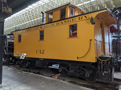 A bright yellow caboose labeled "C12" from the Duluth Missabe & Iron Range Railway, displayed indoors.