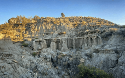 A rugged landscape featuring layered rock formations and sparse vegetation under a clear blue sky.