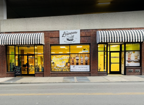 Exterior of The Legendary Milkshake Bar, featuring large windows and striped awnings, with colorful milkshake displays inside.