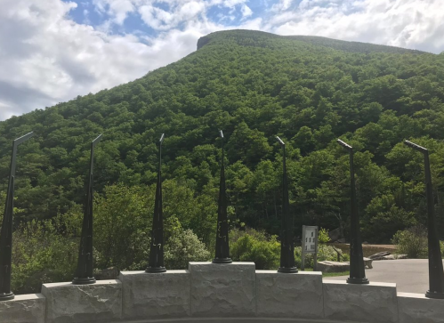 A scenic view of a green mountain under a cloudy sky, framed by tall, black structures in the foreground.
