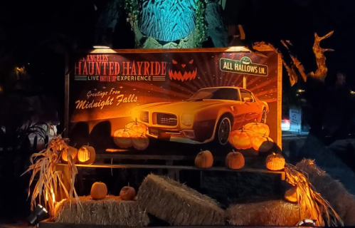 A spooky display featuring a vintage car, pumpkins, and hay bales, promoting a haunted hayride experience.