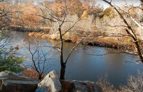 A serene river scene with bare trees and autumn foliage along the banks, reflecting the clear blue sky.