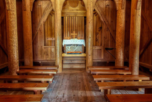 Interior of a wooden chapel featuring an altar, wooden benches, and rustic beams, creating a serene atmosphere.