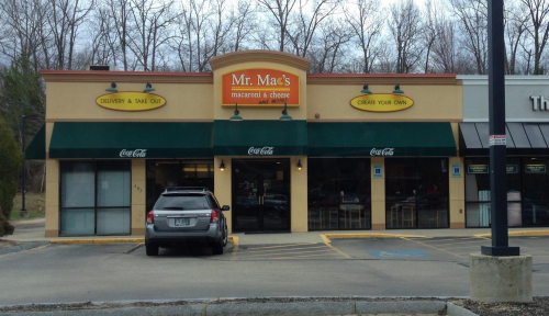 Exterior of Mr. Mac's, a macaroni and cheese restaurant, featuring a delivery sign and outdoor seating.
