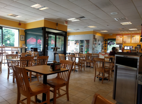 A bright, empty fast-food restaurant with wooden tables and chairs, large windows, and a self-service drink station.