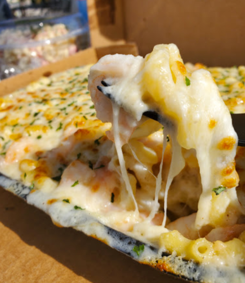 A close-up of cheesy baked pasta with shrimp, featuring gooey melted cheese and a sprinkle of herbs.