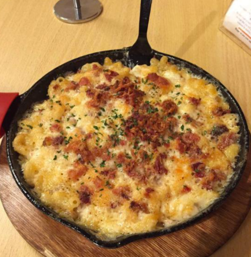 A cast-iron skillet filled with creamy macaroni and cheese, topped with crispy bacon and herbs.