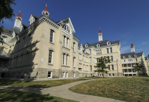 Historic building with ornate architecture, featuring multiple towers and a grassy area in front under a clear blue sky.