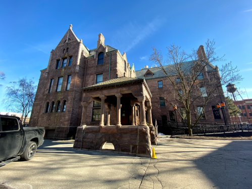 Historic stone building with a turret, featuring a decorative entrance and a black truck parked nearby. Clear blue sky.