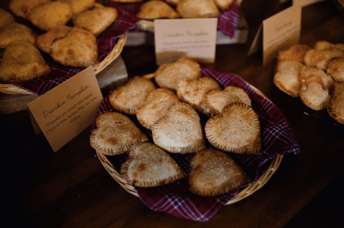 A basket of heart-shaped pastries with a golden crust, displayed on a table with small labels.