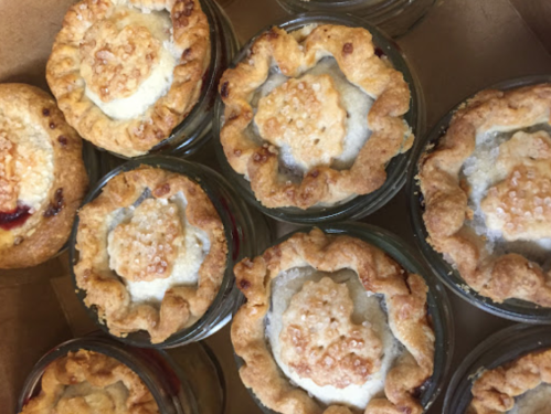 A close-up of mini pies in glass jars, featuring golden crusts and sprinkled sugar on top.