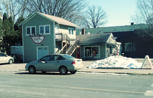 A two-story building with a sign reading "Tasty Treats" and a parked car, with snow piled nearby on a sunny day.