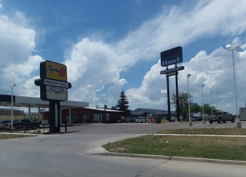 Signage for Super 8 hotel with indoor pool and hot tub, alongside a hotel and restaurant, under a cloudy sky.