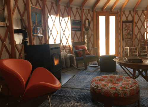 Cozy interior of a yurt featuring a wood stove, colorful seating, and warm lighting.