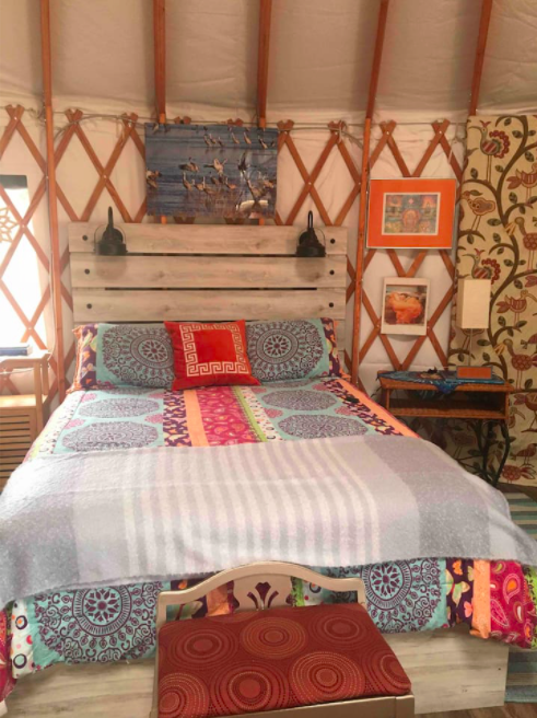 Cozy yurt interior featuring a colorful bedspread, wooden accents, and decorative wall art.