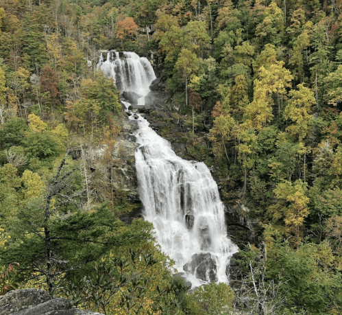A scenic view of a waterfall cascading down rocky cliffs, surrounded by vibrant autumn foliage.