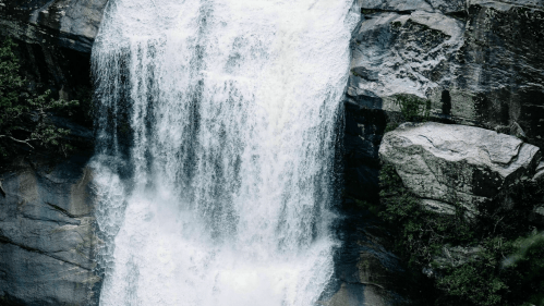 A cascading waterfall flows over rocky cliffs, surrounded by lush greenery.
