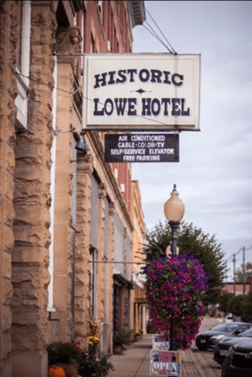 Sign for the Historic Lowe Hotel, featuring amenities like air conditioning, cable TV, and free parking, with flowers below.