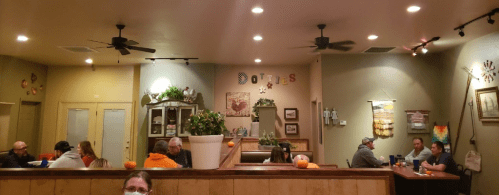 A cozy restaurant interior with patrons seated at tables, warm lighting, and decorative wall art.