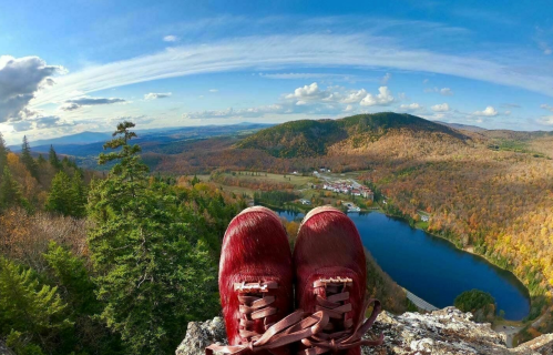 A pair of red sneakers on a rocky ledge overlooking a scenic landscape of mountains and a lake.