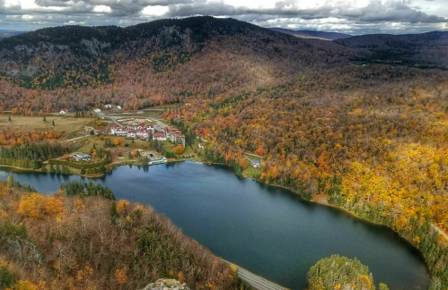 Aerial view of a lake surrounded by autumn foliage and a small resort nestled in the hills.