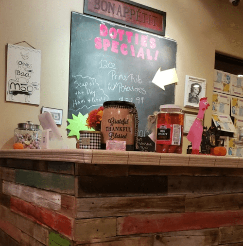 A rustic counter with a chalkboard menu, jars, and decor, featuring a special for prime rib and a colorful display.