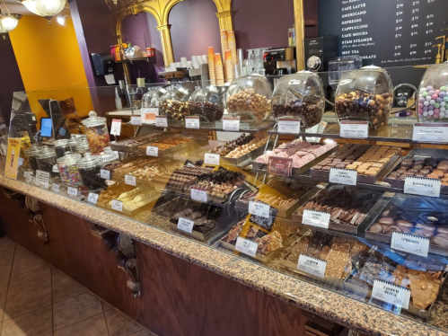 A display case filled with various chocolates, candies, and desserts in a cozy shop setting.