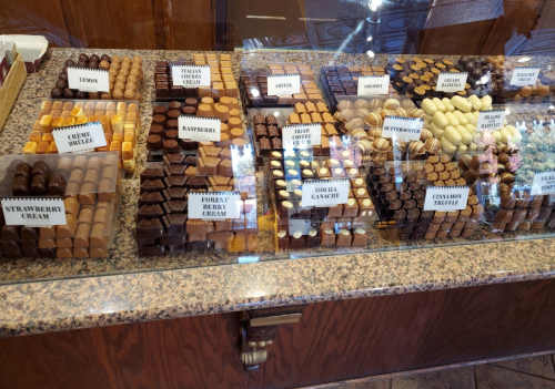 A display case filled with assorted chocolates, labeled with flavors like lemon, raspberry, and coffee.