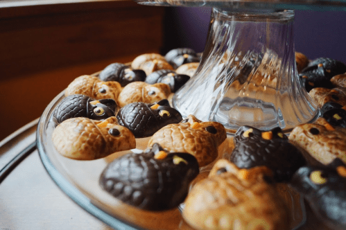 A glass cake stand filled with owl-shaped cookies, featuring brown and black icing and bright yellow eyes.