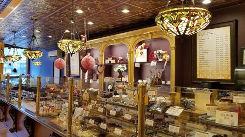 A charming chocolate shop interior with ornate decor, glass displays filled with various chocolates, and decorative lighting.