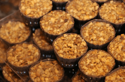 A close-up of small, round desserts topped with crushed nuts in dark chocolate cups.