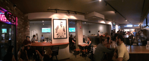 A lively bar scene with patrons enjoying drinks, watching sports on TV, and a vibrant atmosphere.